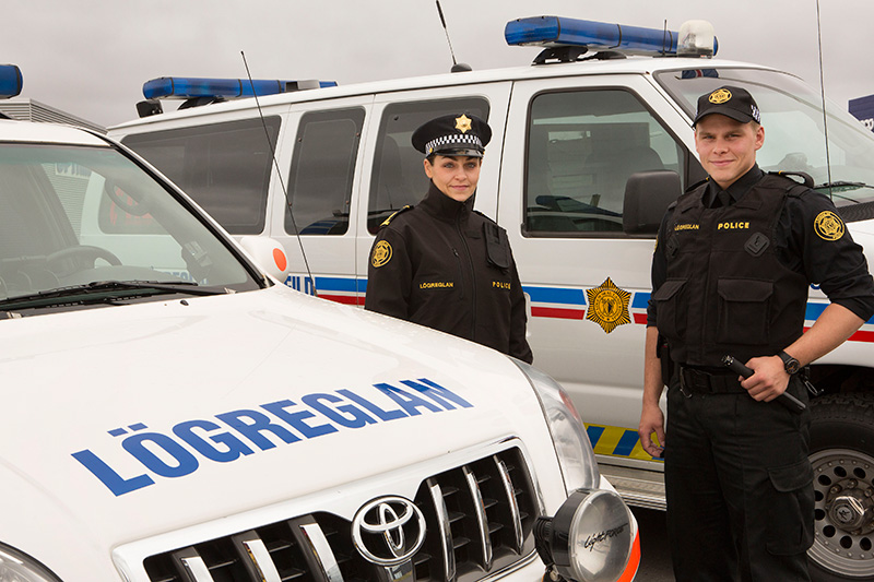Two officers of the Icelandic police pose next to their official vehicles, ready to keep the roads safe and the tourists in check.