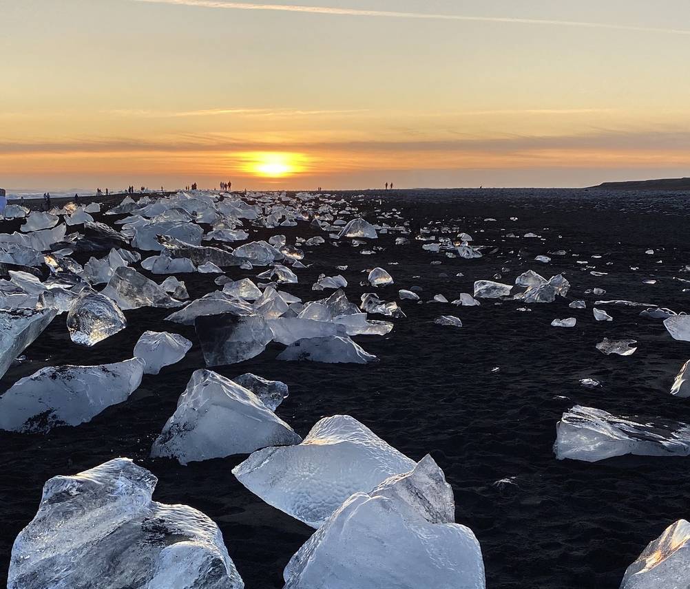 A magical sunset over Diamond Beach in Iceland, with golden light reflecting on the ice blocks resting on the black sand. The combination of warm hues and icy formations makes for a surreal and unforgettable landscape.