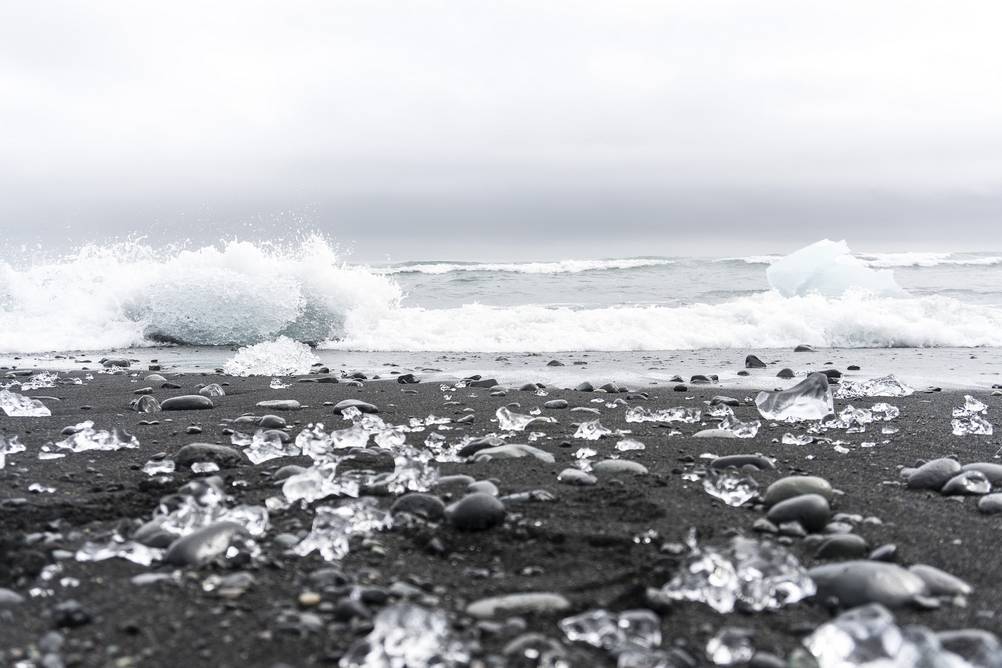 A breathtaking view of Diamond Beach in Iceland, where numerous ice chunks are scattered across the black sand. These ice formations have drifted from the nearby Jökulsárlón glacier lagoon, creating an ever-changing natural wonder