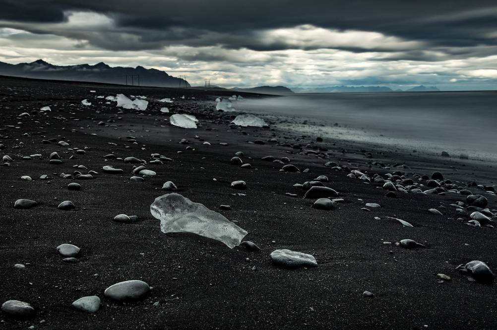 A serene scene of scattered ice chunks along the iconic black sand of Diamond Beach in Iceland, with gentle waves lapping at the shore.