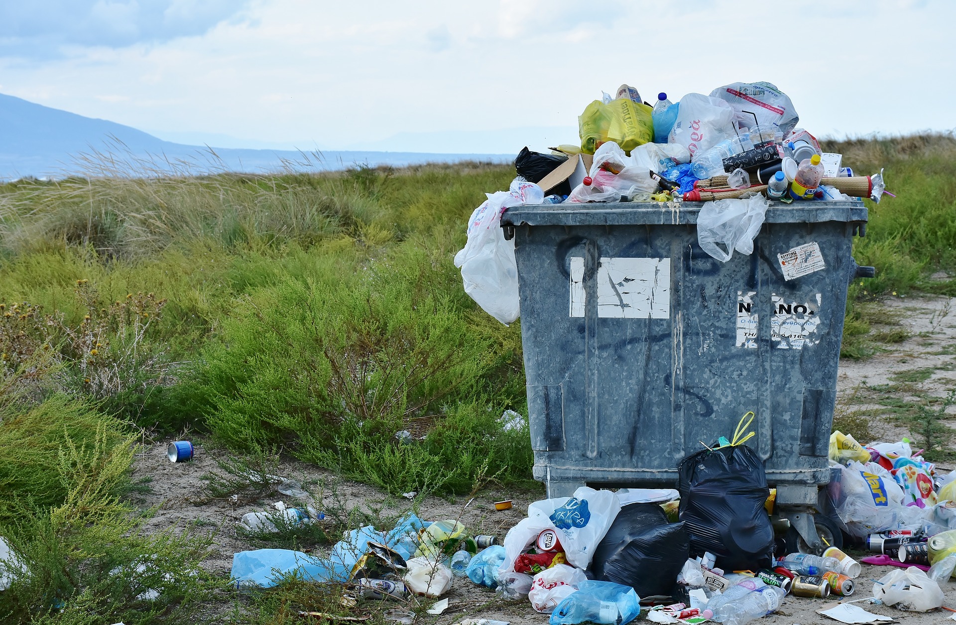A garbage container surrounded by litter in a grassy field, showing the ugly side of tourism when people forget basic camping etiquette.