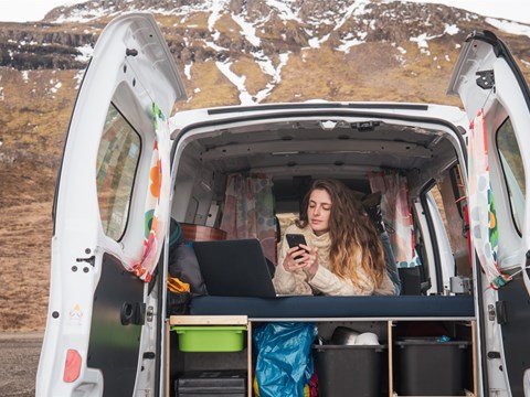 A traveler relaxes inside a well-equipped KuKu campervan, enjoying the stunning Icelandic landscape in the background