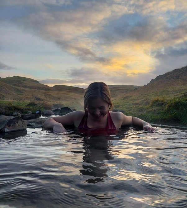 A traveler enjoying the warm waters of Hrunalaug Hot Spring, surrounded by stunning Icelandic landscapes