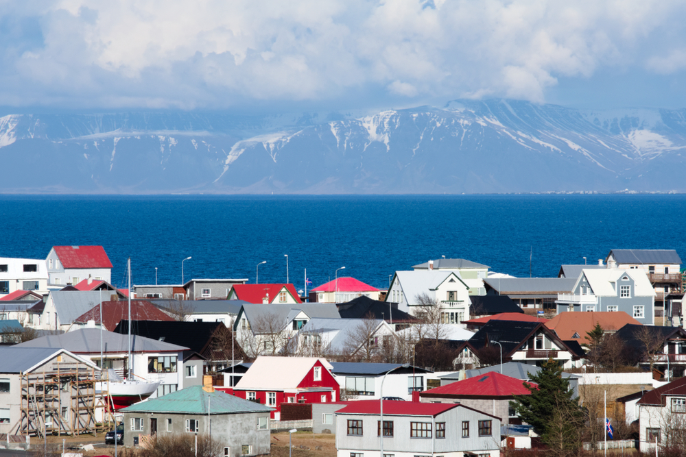 A colorful view of Keflavík town with snowy mountains looming across the ocean – welcome to your Icelandic adventure.