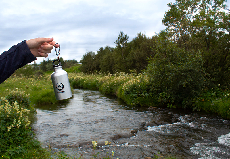 Reusable bottle held over a river in Iceland, promoting easy and eco-friendly water refills during travel.