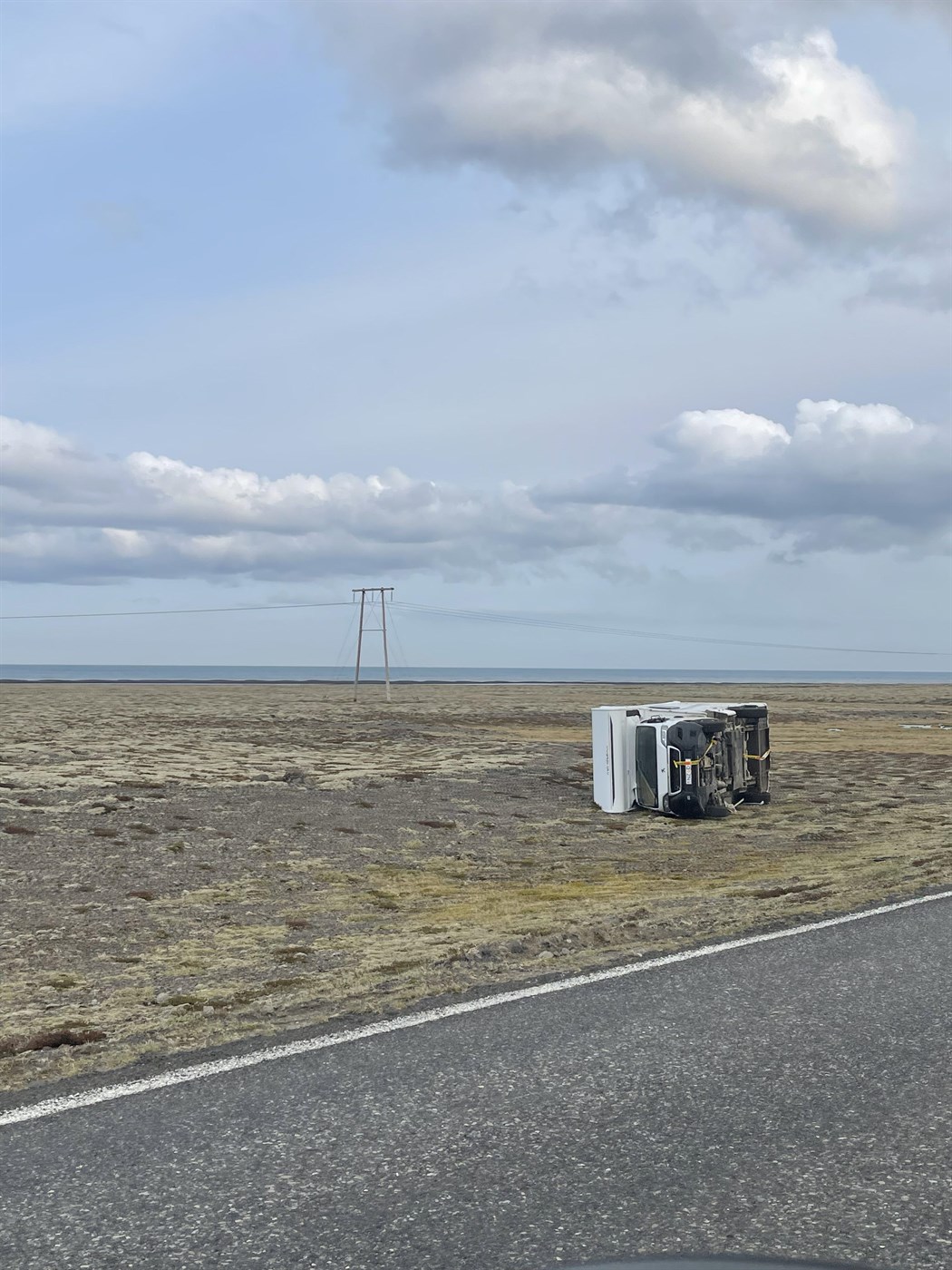 A campervan lies on its side after being overturned by powerful wind in Iceland, showing why door and wind-related damage are not covered by insurance